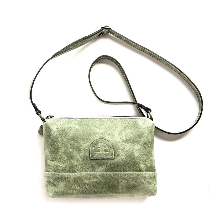 A green leather sling bag with an adjustable strap, displayed against a white background.