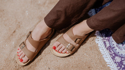 Woman sitting on a sandy beach wearing the Palma sandal